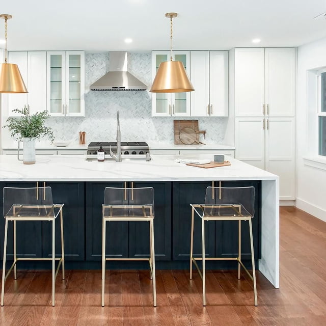 Heavenly Collection Set of 3 Clear Acrylic & Gold Counter Stools with transparent acrylic seats and gold stainless steel bases, placed at a kitchen island with white marble countertop and dark cabinetry, suitable for kitchen seating or dining areas with hardwood flooring and pendant lighting.