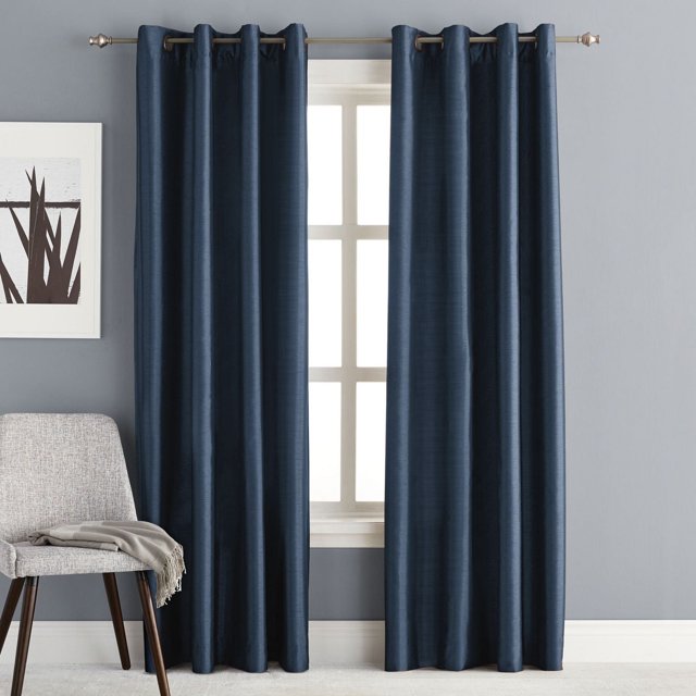 Hometrends Faux Silk Grommet Room Darkening Window Curtains Panel in navy blue with smooth faux silk texture and grommet top, hanging on a metal rod over a window in a gray-walled room with a light gray chair and beige throw, designed to block light, reduce drafts and noise, and save energy.