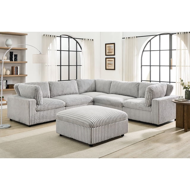K-Living Sectionnel Modulaire Ajustable Colton avec Ottoman en Tissu de Vison, Présenté dans un Salon Lumineux avec des Planchers de Bois Franc Légers et de Grandes Fenêtres Arquées à Cadre Noir. Ce Sectionnel Gris de 6 Pcs Présente un Rembourrage vertical en Velours Côtelé en Tissu de Vison et Comprend un Ottoman Assorti. Son Cadre en Bois Robuste Prend en Charge un design Modulaire Réversible, Idéal pour des Sièges de Salon Personnalisables. la Pièce Comprend des Rideaux Blancs Transparents, une Lampe sur Pied Courbée et une table d'Appoint en Bois avec Déco, Mettant en Valeur le style durable et adaptable du Section