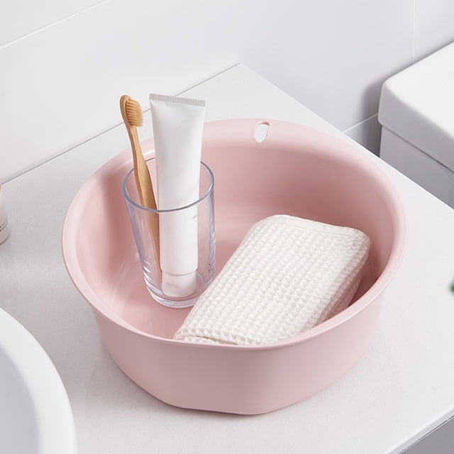 Thickened Plastic Wash Basin in pink, featuring a round flat-bottom design for stability. Measuring 10.43x9.64x3.54 inches, this multi-purpose ABS basin is suitable for laundry, foot baths, and general household use. The image shows the basin placed on a countertop, holding a toothbrush, toothpaste, and a folded white cloth.