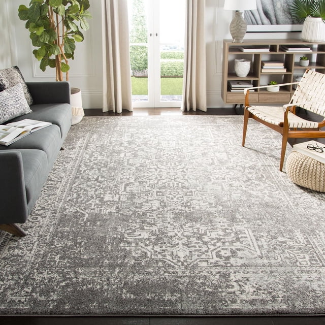 Safavieh Evoke Trena Tapis Traditionnel avec un Motif Gris Atténué et Blanc Cassé Usé, Tissé Mécaniquement à Partir de Fils de Polypropylène à Haute Torsion pour une texture de Frise à Poil Coupé Douce. Exposé sur un Plancher de Bois Franc Foncé entre un sofa Gris et une Chaise en Bois avec des Sangles Blanches Tissées dans un Salon avec des Rideaux Beiges, des Portes en Verre, une console en Bois et une Plante en Pot. Convient pour Ajouter une Touche durable et Stylée aux Zones à Fort Passage.