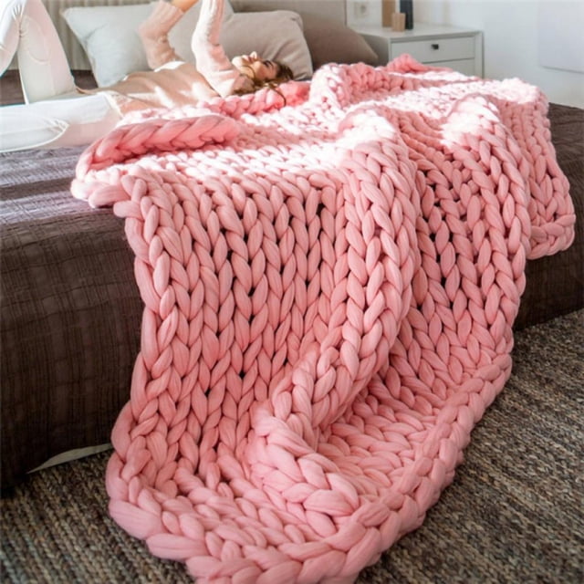 Chunky knit blanket made of soft acrylic fibers in a solid pink color, displayed draped over a bed in a modern bedroom setting. This handmade throw features a boho-inspired design with giant yarn, offering breathability and temperature regulation. Suitable for autumn and winter, it measures 100x120cm (39x47 inches) and is machine washable. Ideal for home decor or as a thoughtful gift.