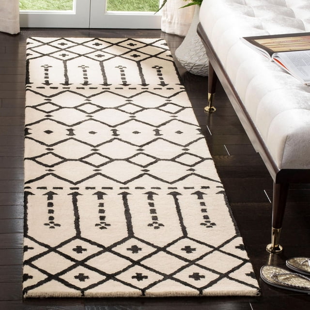 Safavieh Himalaya Darin Geometric Area Rug runner featuring a cream hand-loomed wool base with black geometric patterns, placed on dark hardwood flooring beside a beige tufted bench with brass-capped legs, ideal for hallways and modern home decor, also suitable for layering in entryways.