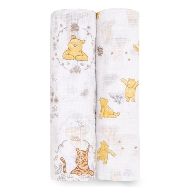 Aden + Anais Essentials 2-Pack Swaddles made of breathable 100% cotton muslin featuring Winnie the Pooh and friends in yellow and brown prints on white fabric, shown rolled side by side, suitable for swaddling, nursing, and stroller covers.