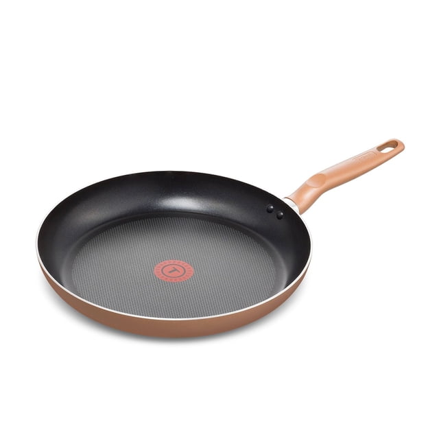 T-fal Essential 32cm Frypan Copper with scratch-resistant non-stick black interior and textured cooking surface featuring a red Thermo-Spot heat indicator, copper-coloured exterior, riveted Bakelite handle with hanging hole, compatible with all cooktops except induction, shown at a 3/4 angle on white background, also suitable for searing and sautéing various foods.