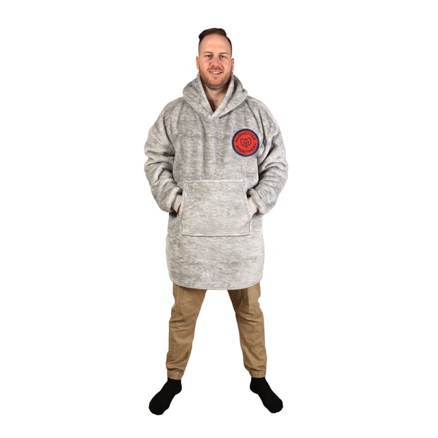 CFL Montreal Alouettes Hooded Wearable Blanket in grey with oversized fit, featuring a sherpa-lined hood, large front kangaroo pocket, and red Montreal Alouettes logo on the chest, worn with tan pants and black socks, ideal for cozy indoor use.