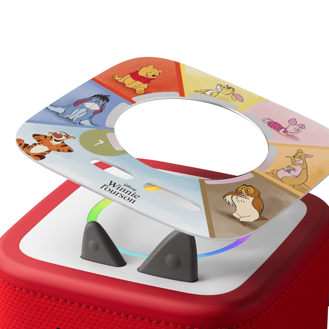 tonies Tonieplay Disney Winnie the Pooh: Tigger's Mix-Up Fix-Up Game (French) showing a circular game disc with colorful segments featuring Winnie the Pooh characters including Pooh, Tigger, Eeyore, Rabbit, Piglet, Kanga, Roo, and Owl around a central hole, placed on a red Toniebox 2 with a white top and two black triangular buttons, illuminated by a multicolor light ring, designed for interactive, screen-free French language play for children ages 3 and up.