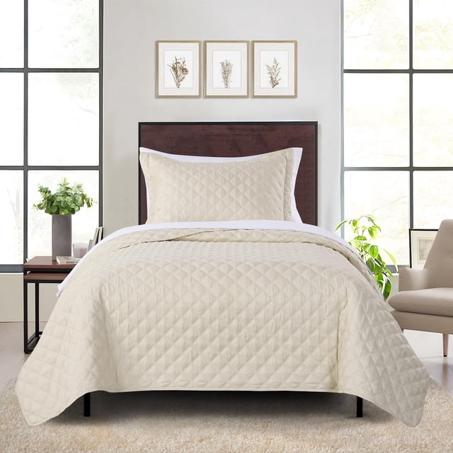 Mainstays Quilt-in-a-Bag Bedding Set in beige featuring a diamond-quilted lightweight quilt and matching pillow sham on a twin bed with dark wood headboard, set in a bright room with large windows, botanical prints, side table with plant, and beige armchair, ideal for year-round use.