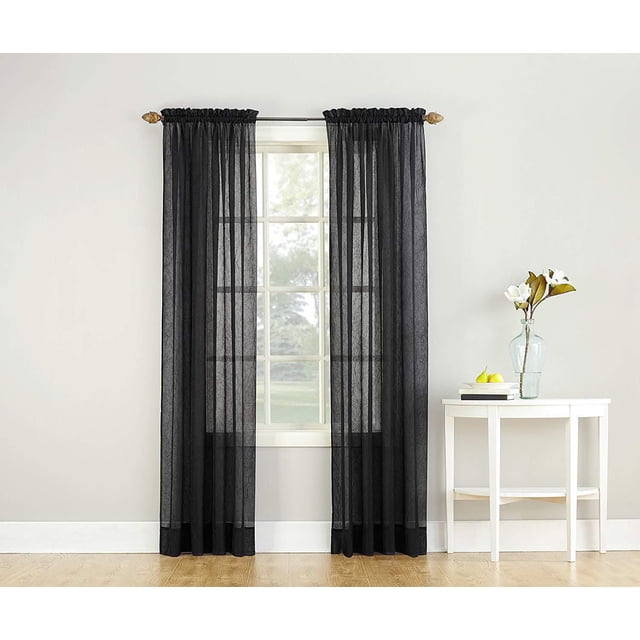 SUN TEXTILE CRUSHED ROD POCKET CURTAIN in black crushed sheer voile fabric with a textured crinkled finish, hanging on a rod pocket over a window, softly filtering light and providing privacy, shown in a neutral room with a white side table holding a glass vase with flowers and books.