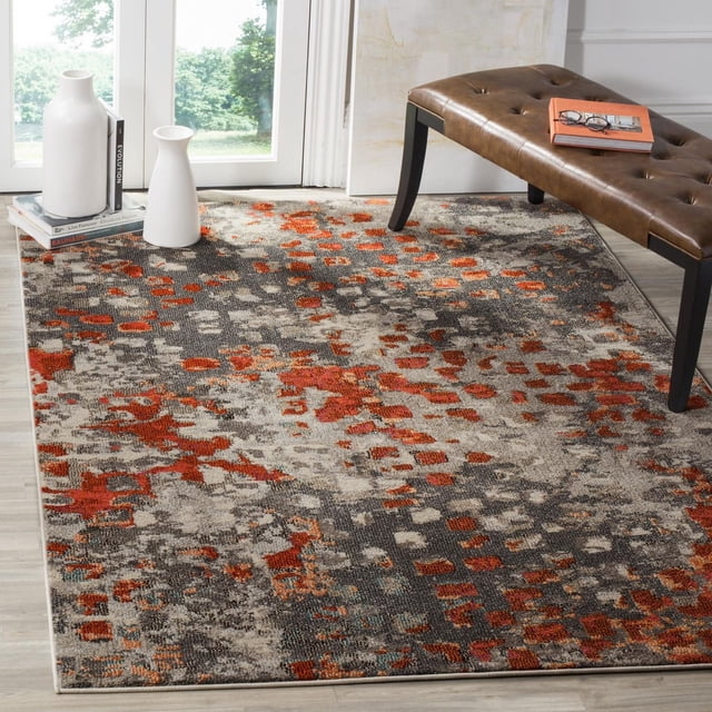 Safavieh Monaco Driskoll Abstract Area Rug with a durable power-loomed polypropylene construction and mixed high and low loop pile, displaying an abstract pattern in orange, gray, and beige tones on light wood flooring beside a brown tufted leather bench and white ceramic vases, ideal for adding Bohemian-chic flair to home interiors.