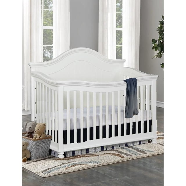 Concord Baby Brayden Lit de Bébé 4-en-1 en Bois Massif Blanc avec Tête de Lit Arquée et rails Inclinés, avec Hauteurs de Matelas Ajustables et design convertible du Lit de Bébé au Lit pour Tout-Petit, Montré avec une Couverture Bleu Foncé sur le Côté, Placé sur un Tapis à Motifs avec des Animaux en Peluche dans une Chambre de Bébé.
