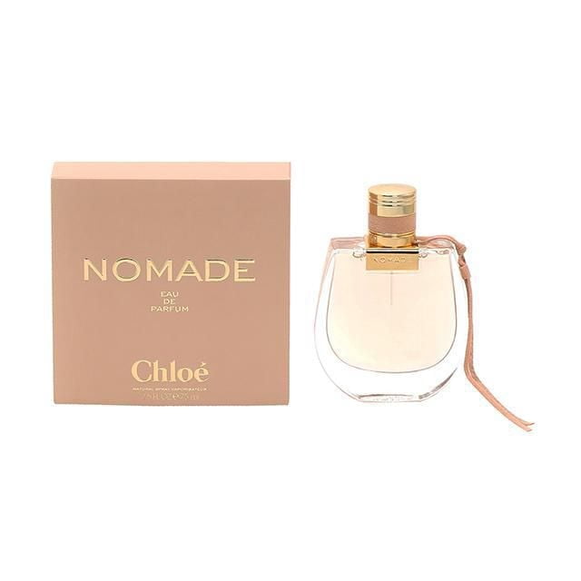 Chloe Nomade Eau De Parfum Spray For Women 75ml featuring a clear glass bottle with a rounded rectangular shape, gold-tone cap, and beige leather strap, next to a beige box with gold embossed Nomade and Chloé branding, representing a citrus musky woody fragrance.