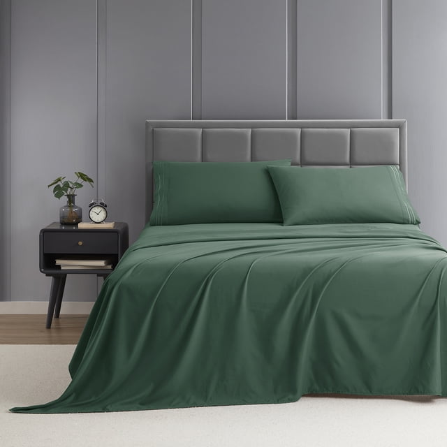 Nestl King Sheet Set, 1800 Series Microfiber Deep Pocket 4 Piece Bed Sheet Set displayed on a neatly made bed. The set includes a fitted sheet, flat sheet, and two pillowcases in a deep green color. The bed is styled in a modern bedroom with a grey upholstered headboard, a black nightstand holding a clock and plant, and a neutral carpeted floor. The microfiber fabric is double-brushed for softness, resistant to pilling, and features a classic stripe detail for an elegant look.