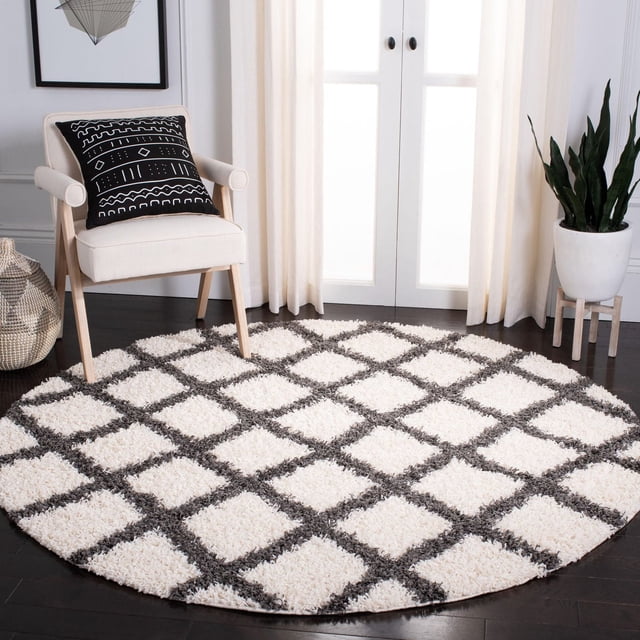 Safavieh Dallas Jerrie Tapis Shag Géométrique pour Aire, Rond avec Fibres Synthétiques Blanches Moelleuses et Motif Losanges Gris Foncé, Posé sur Plancher de Bois Franc Foncé dans une Pièce Lumineuse avec un Fauteuil beige Présentant un Coussin Géométrique Noir, des Rideaux Blancs et une Plante Serpent dans un pot Blanc sur un Support en Bois, Idéal pour les Zones à Fort Achalandage.