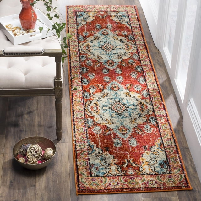 SAFAVIEH Monaco Toria Traditional Area Rug runner featuring vintage oriental orange and light blue distressed patterns on a durable polypropylene power-loomed pile, placed on hardwood flooring beside a beige upholstered chair and decorative bowl with woven natural spheres, suitable for adding bohemian-chic flair to hallways or entryways.