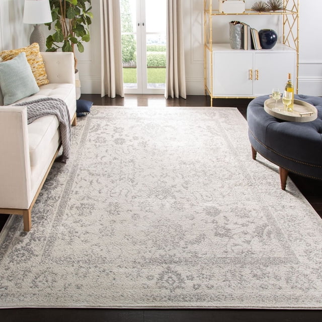 SAFAVIEH Adirondack Wyatt Tapis Traditionnel pour Aire en Gris Pâle et Crème avec Motif floral Surteint, Fait de Fils de Polypropylène Durables. Positionné sur des Planchers de Bois Franc Sombres entre un sofa beige et un ottoman Capitonné Bleu Marine dans un Salon Naturellement Éclairé, Ce Tapis Reflète un style Rustique de Chalet et Convient aux Maisons de Campagne et de Ville.