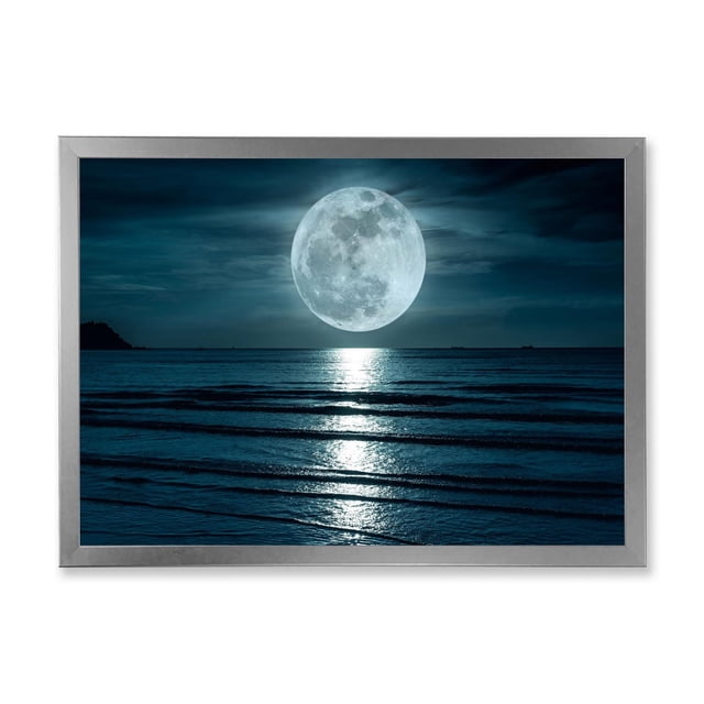 Designart Super Moon Over The Sea I Framed Wall Art depicting a large full moon reflecting on ocean waves beneath a dark blue night sky, printed on fade-resistant cotton canvas and mounted in a 1.5-inch silver frame, suitable for modern home décor and canvas prints.