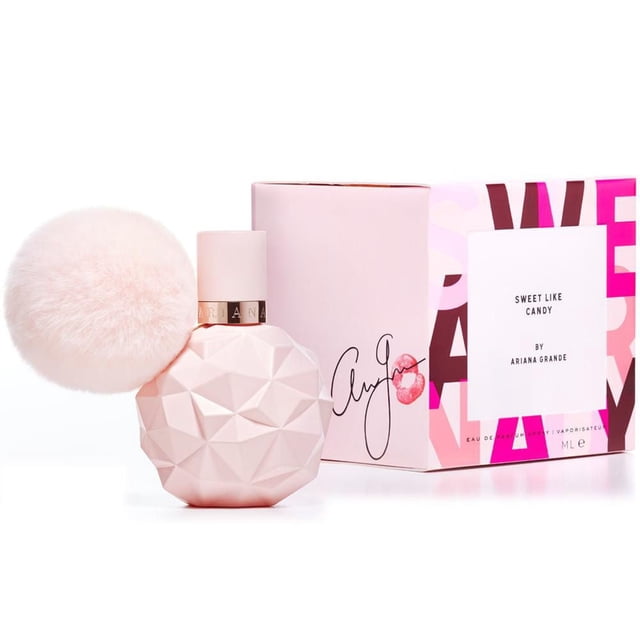 Ariana Grande Sweet like Candy Vaporisateur Eau de Parfum 100 ml avec une Bouteille Rose Pâle Facettée et un Grand Pompon Rose Doux sur le Cou, Exposé avec Sa Boîte Rose Présentant un Texte Multicolore Audacieux et une Étiquette Blanche avec le Nom et la Marque du Parfum, Convient aux collections de Parfums pour Femmes.