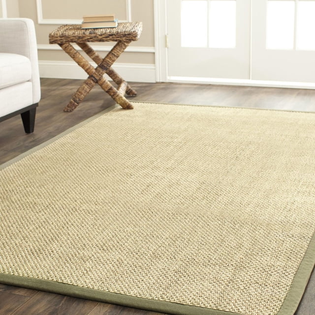 Safavieh Natural Fiber Juniper Border Area Rug in beige woven sisal with a green fabric border, placed on hardwood flooring beside a wicker side table and grey upholstered chair in a bright room, ideal for coastal or casual beach house style interiors.