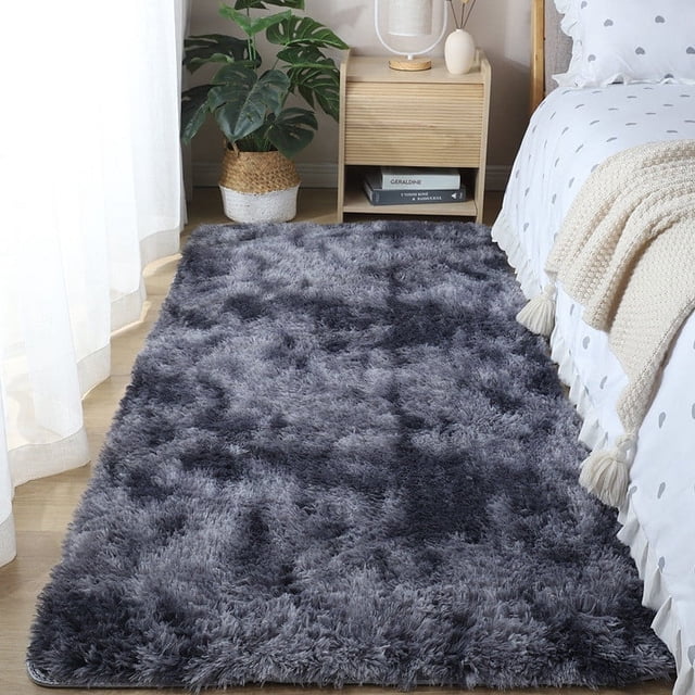 Boovnll Rugs for Bedroom, a super soft and cozy tie-dyed plush throw rug measuring 2x5.2 feet, displayed beside a bed in a modern bedroom. The rug features a dark grey tie-dyed pattern with a thick, artificial fleece surface and a non-slip bottom. Ideal as a runner rug or area rug for living rooms, bedrooms, and home decor.