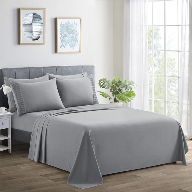 Marina Decoration Ultra Soft Silky Deep Pocket Solid Rayon from Bamboo Bedding All Season Sheet Set in grey on a bed with a grey upholstered headboard. The set includes a fitted sheet with elastic deep pockets, flat sheet, and pleated pillowcases. The room features light wood flooring, white walls with two framed abstract prints, a white nightstand with a lamp and cup, and a green plant by a large window with sheer curtains, highlighting breathable, wrinkle-resistant bedding ideal for year-round comfort.