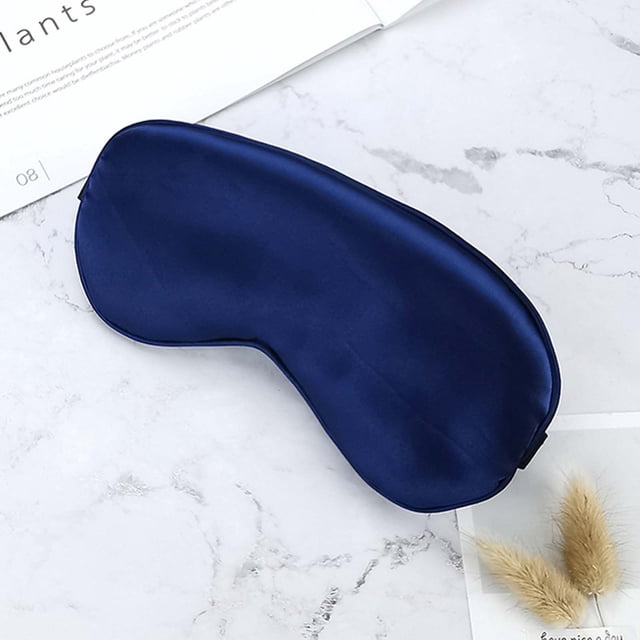 PVCS Sleep Mask Silk Blackouted Soft Travel Mask with Adjustable Strap Sleep Eye Mask. A dark blue silk sleep mask with a smooth texture, designed to block out light for restful sleep. Features an adjustable elastic strap for a secure and comfortable fit. Lightweight and hypoallergenic, suitable for all head sizes, including children. Displayed on a marble surface with decorative elements in the background.