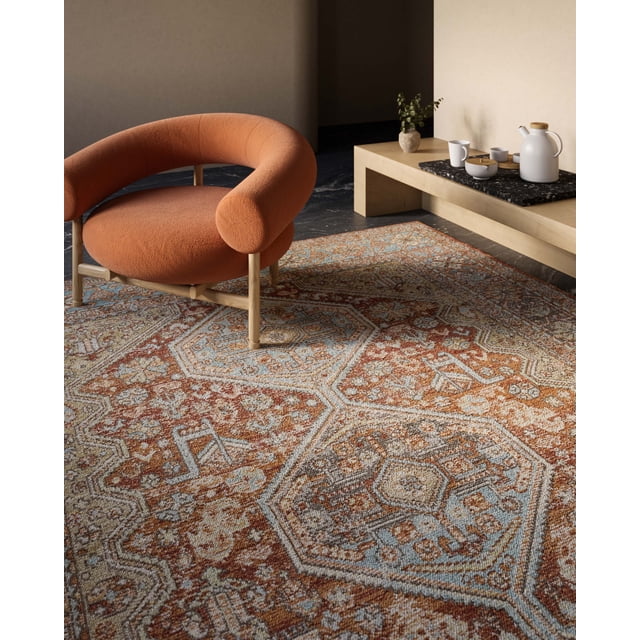 ECARPET Alicia Traditional Area Rug with warm copper and blue vintage geometric patterns, displayed in a sunlit room with a curved orange upholstered chair and a low wooden table holding a white ceramic tea set and a small vase with greenery, suitable for living rooms, bedrooms, or entryways.