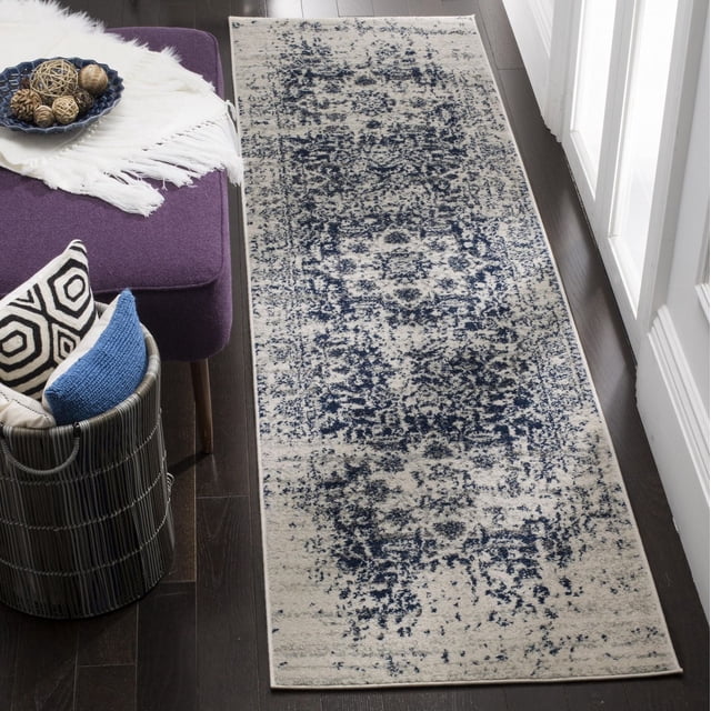 Safavieh Madison Katina Traditional Faded Area Rug runner measuring 2'3" x 12' with a transitional faded navy blue and beige pattern on durable yarn, displayed on dark hardwood flooring next to a purple upholstered bench and a basket with decorative cushions, suitable for hallways or entryways.