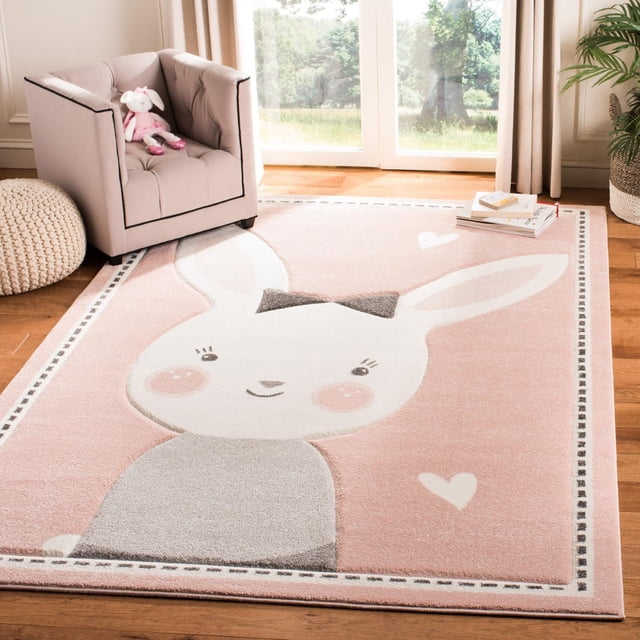 Safavieh Carousel Kids Tapis Clark Timide Bunny pour Aire avec un Fond Rose pastel Mettant en Vedette un Grand Bunny Blanc avec un Nœud Gris et des Joues Rosées, Bordé d'Un Motif Cousu, Posé sur un Plancher de Bois Franc dans une Chambre d'Enfant avec un Fauteuil beige et une Peluche, Idéal pour une Déco durable et Douce pour Enfants.