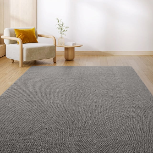 Mainstays Washable Finley Diamond Wild Dove Tufted 6'x8' area rug featuring a textured grey diamond pattern made from 100% recycled, stain-resistant polypropylene yarn with eco-friendly TPE non-slip backing, displayed on light hardwood flooring near a beige armchair with a mustard yellow pillow and a round wooden side table with a glass vase and books, ideal for entryways, kitchens, or living rooms.