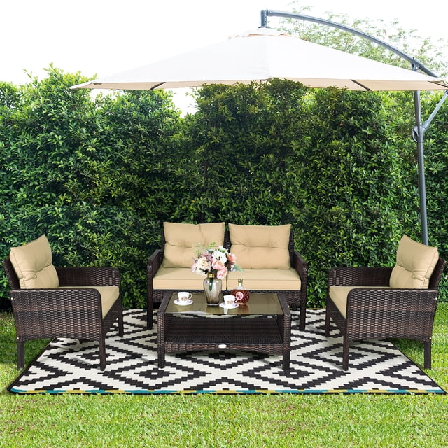 Costway Ensemble de Mobilier de Patio en Rotin 4 Pcs avec une Causeuse, Deux Chaises Simples et une table Basse avec Dessus en Verre Trempé. Comprend des Coussins Beiges pour le Confort. Exposé à l'Extérieur sur un Tapis à Motifs Entouré de Verdure Luxuriante, Parfait pour le Jardin, la Cour Arrière Ou les Sièges de Patio.