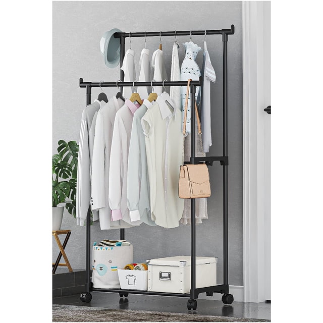 Tyidzon Clothing Rack, a black metal garment rack with double rods for hanging clothes, shown in a modern interior setting. The rack features a bottom shelf for shoes and storage boxes, sturdy wheels for mobility, and a compact design measuring 130cm in height, 60cm in length, and 35cm in width. It is organized with shirts, dresses, and accessories, making it suitable for bedrooms, laundry rooms, or living rooms.