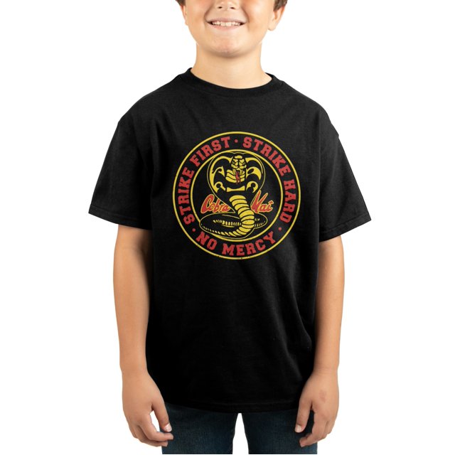 Cobra Kai Logo Kids Black T-Shirt featuring the iconic Cobra Kai logo with the text 'Strike First, Strike Hard, No Mercy' in bold red and yellow accents. Made from 100% lightweight cotton, this officially licensed Bioworld t-shirt is designed for comfort and durability. The shirt is shown worn by a child, highlighting its relaxed fit and casual style.