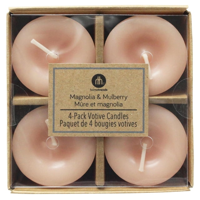 Hometrends Magnolia & Mulberry Scented 4-Pack Votive Candles centered front-facing view of four blush-colored wax votive candles grouped tightly; short cylindrical silhouette with visible centered cotton wicks and smooth finish; one base edge shows HOMETRENDS text; placed on a neutral tabletop suggesting mantel or tabletop use; Magnolia & Mulberry fragrance as stated; often used as small decorative accents or included in gift sets.