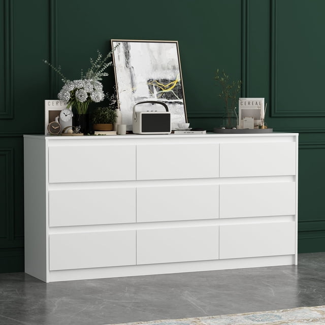 OXYLIFE Commode Blanche à 9 Tiroirs, une Commode en Bois avec un design d'Organisateur de Rangement vertical, Présentée dans un Cadre de Pièce Moderne. la Commode Présente une Finition Mate Blanche sur un Cadre en MDF Laminé et en Panneau de Particules, Complétée par des Pieds en Bois Tournés. Elle Comprend Neuf Tiroirs Spacieux pour Organiser des Vêtements, des Accessoires Ou des Jouets. la Commode Présente un Style avec des Articles Décoratifs sur le Dessus, Y Compris une Oeuvre Encadrée, des Livres et des Plantes, contre un Mur Vert Foncé. Idéale pour les Chambres, les Salons