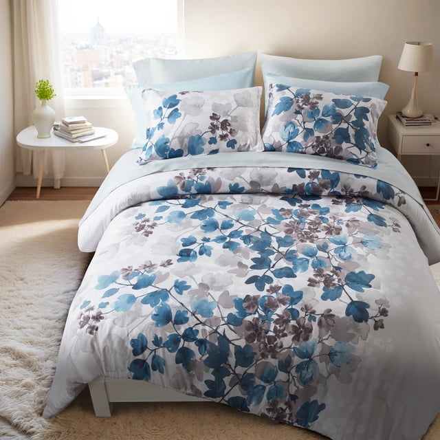 Regency Heights King Size Comforter Sets, featuring a blue botanical floral design with shades of white and gray on ultra-soft microfiber. The set includes a comforter, two king shams, a flat sheet, a fitted sheet with two 8" x 9" side pockets, two king pillowcases, and two bonus pillowcases. Displayed in a cozy bedroom setting with a white bed frame and a light-toned rug, the bedding adds a modern and elegant touch to the decor.