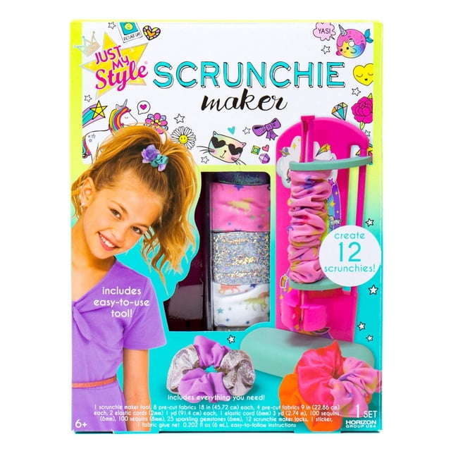 Just My Style D.I.Y. Scrunchie Maker kit with a pink scrunchie maker tool holding a pink fabric scrunchie, six colorful pre-cut fabric strips including glitter and patterned designs, and three finished scrunchies in purple, silver, and pink. The kit allows creating 12 scrunchies with easy-to-use tools and accessories, ideal for kids aged 6 and up in arts and crafts.