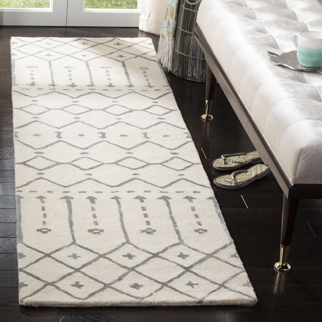 Safavieh Himalaya Darin Geometric Area Rug runner with cream base and light gray geometric patterns, crafted from 100 percent hand-loomed wool, shown on dark hardwood floor beside a beige tufted bench with gold-capped legs, suitable for modern hallways and entryways.