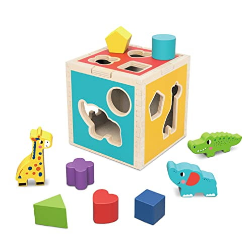 TOOKYLAND Wooden Shape Sorter Cube Toy featuring a multicolour wooden cube with cutouts for various shapes and animal figures. Includes 9 sorting blocks in geometric shapes and animal designs such as a giraffe, elephant, and crocodile. Designed for toddlers aged 12 months and up, this Montessori toy promotes fine motor skills, shape and colour recognition, and problem-solving. Made of non-toxic, smooth-surfaced wood for safe play.