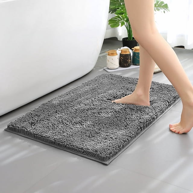 Hitime Soft Chenille Bath Mat Grey 20x30 placed on a bathroom floor, featuring a plush chenille texture in dark gray. A person steps onto the ultra-absorbent, quick-drying mat, which has a non-slip TP rubber backing for stability. Ideal for bathrooms, showers, or hallways, this machine-washable rug adds warmth and comfort while protecting floors.