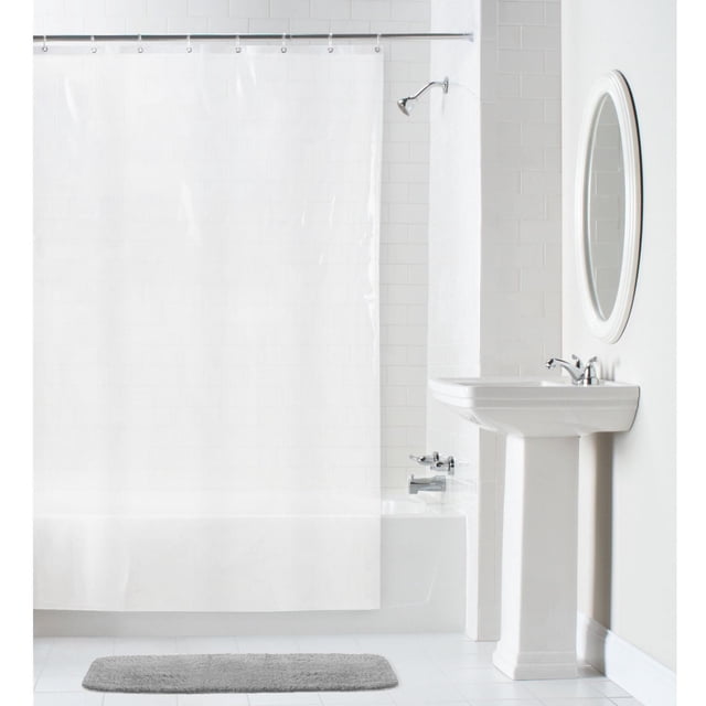 Mainstays Waterproof Heavyweight PEVA Shower Curtain Liner in clear translucent PEVA with rustproof metal grommets and reinforced mesh header, hanging on a silver rod inside a white tiled bathtub and shower area, accompanied by a white pedestal sink and oval mirror, with a gray bath mat on the white tiled floor, designed for mildew resistance and easy maintenance.