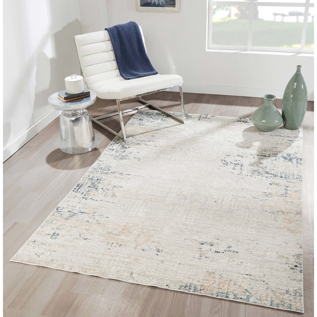 ECARPET Amber Traditional Area Rug in ivory with weathered blue-gray geometric and tribal patterns, placed on light hardwood flooring in a bright room with a white leather chair with chrome legs, a metallic side table with books and a candle, and two green ceramic vases near a large window, ideal for high-traffic living areas.