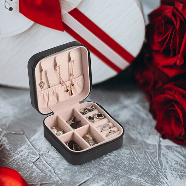 TopLLC Earring Ring Jewelry Display Storage Box Case Organizer Flannel Tray Holder Gift in a compact square design with a black exterior and soft beige interior. The open box reveals multiple compartments for organizing earrings, rings, necklaces, and other accessories. The lid features necklace hooks and a net pocket for added storage. The box is displayed on a decorative surface with red roses and a white gift box in the background.