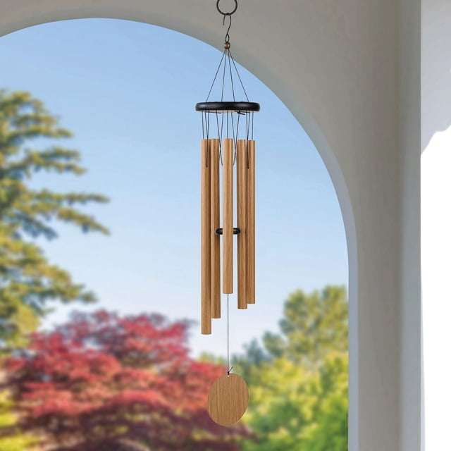Hometrends 30 Pouces Classique Naturel Faux Pin Métal Extérieur Wind Chime Suspendu à un Anneau en Métal Noir sous une Arche Blanche, avec Cinq tubes Ton Bois Naturel et un Capteur de Vent Rond en Bois, sur un Fond Flou d'Arbres Verts et Rouges sous un Ciel Bleu Clair.