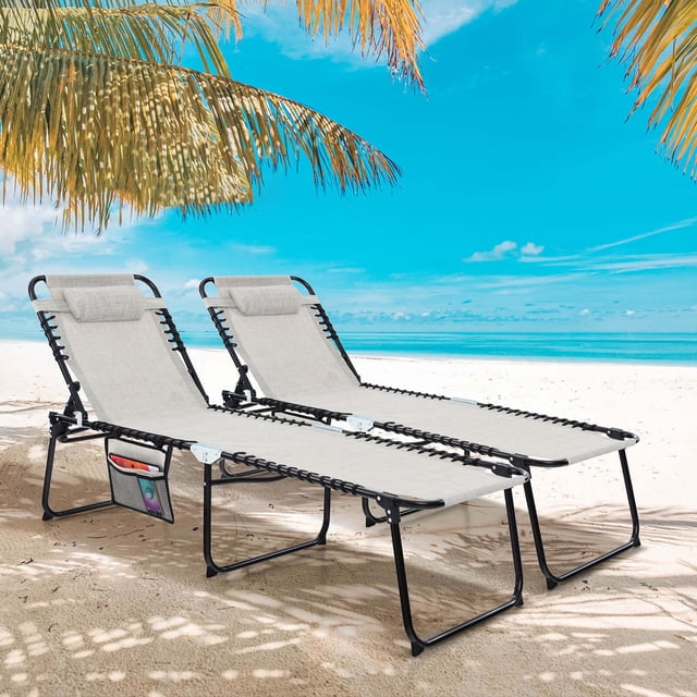 Costway 2 PCS Folding Chaise Lounge Chair Portable Sun Lounger with Adjustable Backrest Grey. Two grey outdoor lounge chairs with breathable fabric and sturdy metal frames, featuring adjustable backrests, detachable headrests, and side pockets for storage. Ideal for patio furniture, positioned on a sandy beach under palm trees with a clear blue sky in the background.