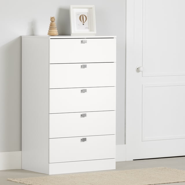 South Shore Spark Commode à 5 Tiroirs pour Enfant en Blanc Pur avec Cinq Tiroirs Spacieux sur Glissières en Métal et Poignées Carrées en Métal, Montrée Orientée vers l'Avant contre un Mur Gris Pâle à Côté d'Une Porte Blanche, Surmontée d'Un Jouet Empilable en Bois et d'Un Imprimé de Montgolfière Encadré, Idéale pour Organiser les Vêtements des Enfants et Maximiser le Rangement de la Chambre.