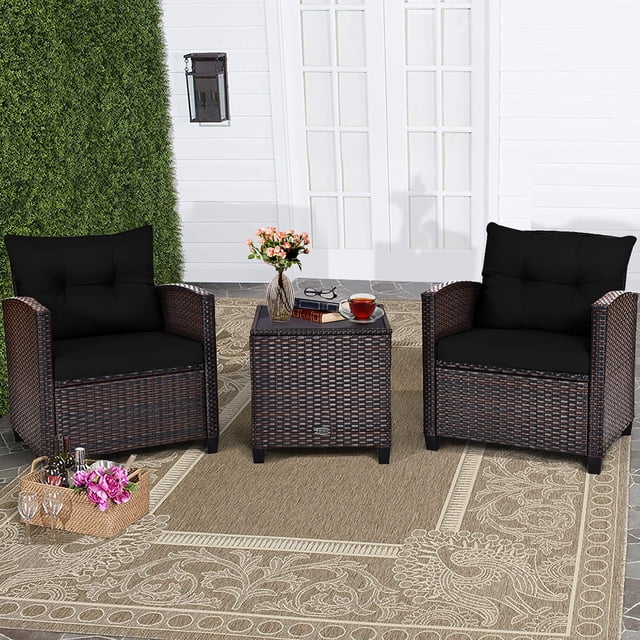 Costway 3PCS Patio Rattan Furniture Set Cushion Conversation Set Sofa Coffee Table Black. The set includes two single rattan sofas with black cushions and a square coffee table with a tempered glass top. The furniture features a mix brown rattan design and is displayed on a beige patterned outdoor rug in a patio setting with greenery and a white wall in the background. Ideal for outdoor spaces like patios, gardens, or poolside areas.