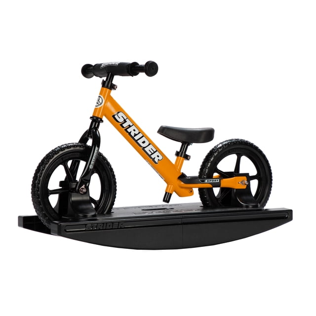 Strider 12 Sport 2-in-1 Rocking Bike in orange, designed for children aged 6 months to 5 years. The bike is securely mounted on a black rocking base, allowing babies to rock safely while developing balance and coordination. The lightweight frame features toddler-sized grips, a cushioned seat, and no-tool adjustable handlebars and seatpost. The bike can be detached from the base for use as a balance bike, with never-flat tires and a seat height range of 30-48 cm (11-19 in.), suitable for children with an inseam of 22-51 cm (8.75-20 in.).