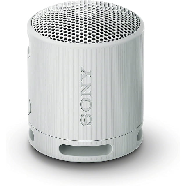 Sony SRS-XB100 Waterproof Bluetooth Wireless Speaker in light grey, featuring a compact cylindrical design with a textured finish and a perforated metal grille on top. This portable speaker offers powerful, clear sound with deep bass, a waterproof and dustproof IP67 rating, and up to 16 hours of battery life. It includes a versatile strap for easy carrying and a USB Type-C port for charging. Compatible with Bluetooth streaming and stereo pairing with a second speaker.