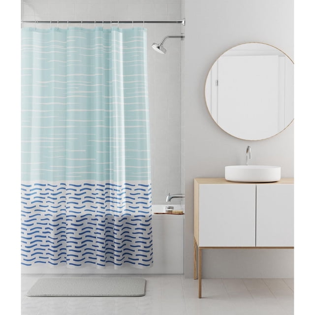 Mainstays Decorative Waterproof Recycled PEVA Shower Curtain featuring light blue and white horizontal lines on the upper half and dark blue wave patterns on the lower half, sized 70 by 72 inches to fit standard bathtubs, hanging on a metal rod above a white bathtub with a silver showerhead, next to a wooden vanity with a round mirror and white vessel sink, on a tiled floor with a gray bath mat, ideal for bath décor with easy-to-clean waterproof recycled material.